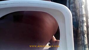 African woman bangs herself with a toy while bent over on the chair