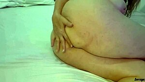 Sogra creates a video applying cream all over her body in a simple bedroom setting.